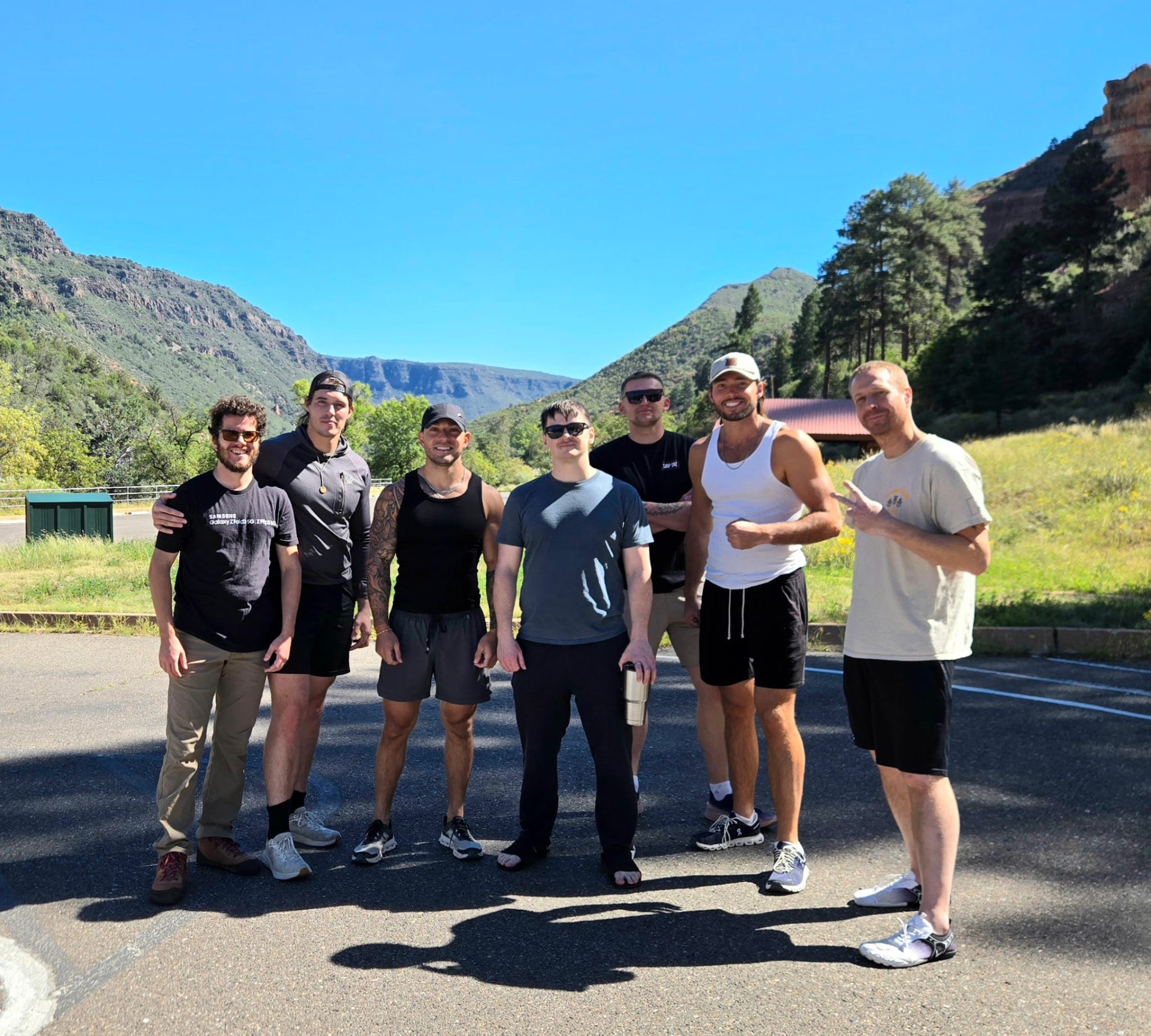 Seven men standing together beneath canyon cliffs and pine trees