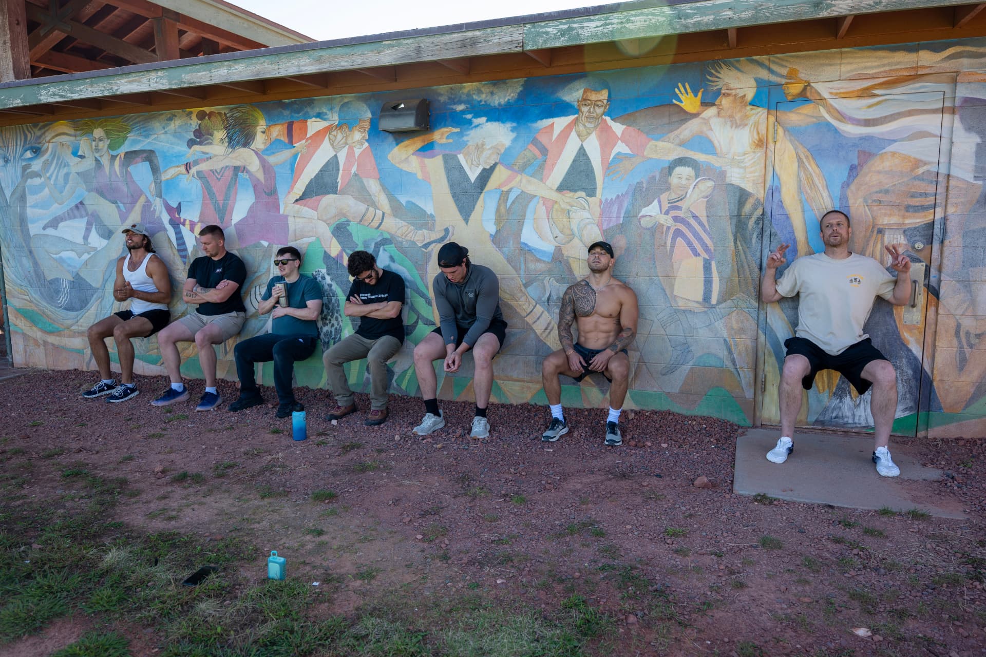 A group holding a wall sit together in front of a painted mural